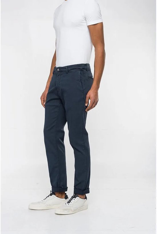 Man met donkerblauwe chino broek, omgeslagen broekspijpen en witte sneakers, zijaanzicht.