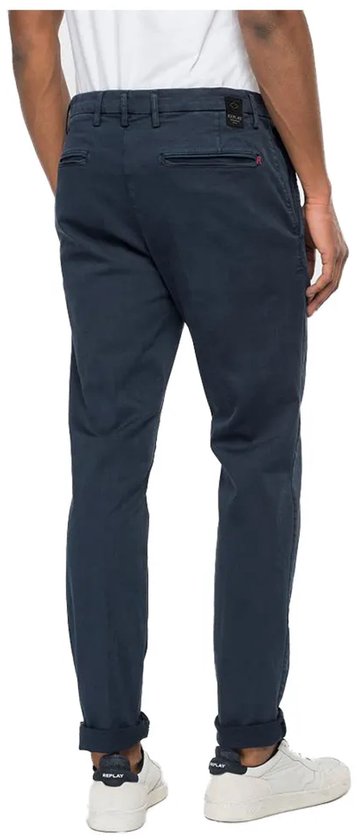 Achterkant man met donkerblauwe chino broek, omgeslagen broekspijpen en witte sneakers.