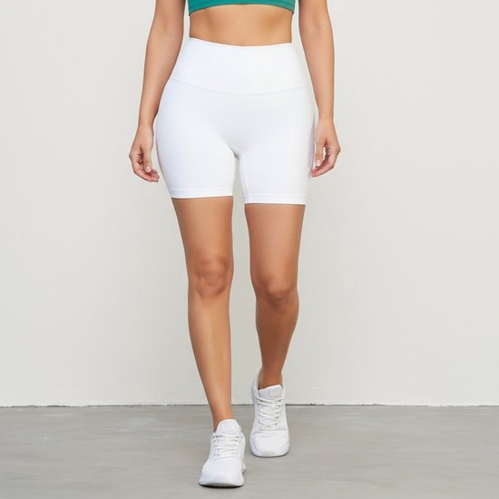 Een model in een witte, hoge taille yoga short en een groene sportbeha.