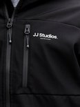 Detail van een zwarte jas met ritsen, 'JJ Studios. Jack & Jones' logo en een ritszakje.