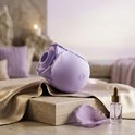 Lila rozenvormige vibrator op satijnen stof, met een rozenblaadje en olieflesje.