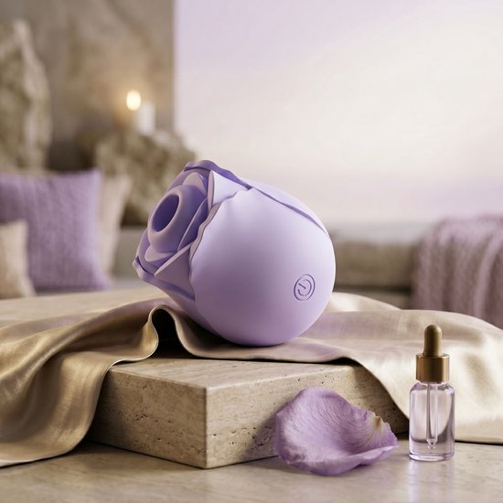 Lila rozenvormige vibrator op satijnen stof, met een rozenblaadje en olieflesje.