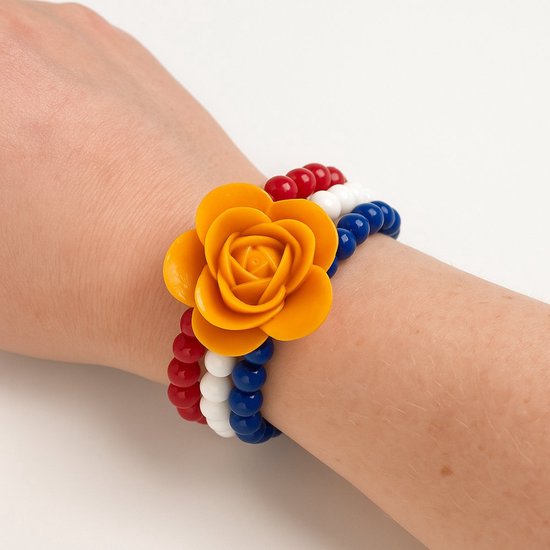 Een armband met rode, witte en blauwe kralen en een oranje bloem gedragen om een pols.