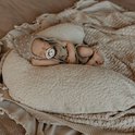 Pasgeboren baby slaapt op een beige voedingskussen, draagt een beige mutsje met pompon.