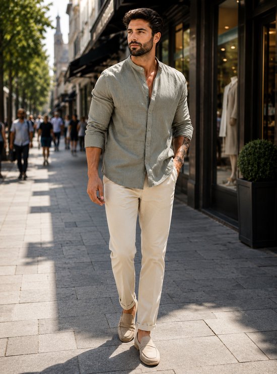 Man loopt over straat met de voorkant naar de camera, draagt een lichtgroene linnen blouse en beige broek.