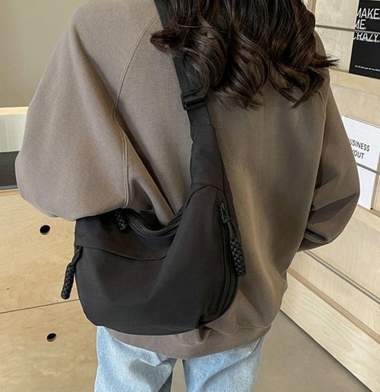 Zwarte crossbody tas, gedragen over de schouder, met een gedraaide ritstrekker aan de zijkant.