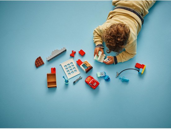 LEGO Duplo onderdelen: rode Lightning McQueen auto, garage, doktersspullen en gereedschap, uitgestald op blauwe ondergrond.