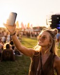 Vrouw met zonnebril neemt selfie met zonnepaneel powerbank bij zonsondergang.