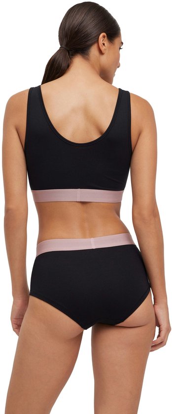 Een vrouw staat met de rug naar de camera in een zwarte sportbeha en broek met roze FALKE-band.