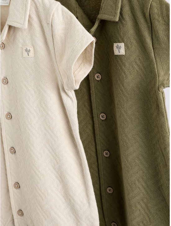 Close-up van beige en groene babyrompertjes met visgraatpatroon en knopen.