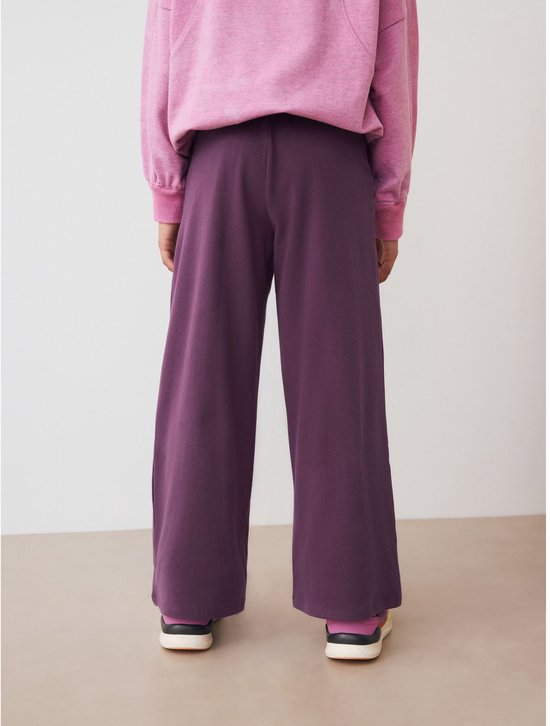 Achterkant van een kind dat een paarse wijde tricot broek en roze trui draagt.