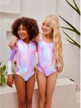 Twee meisjes die poseren, beiden in veelkleurige badpakken met tie-dye print en pailletten.