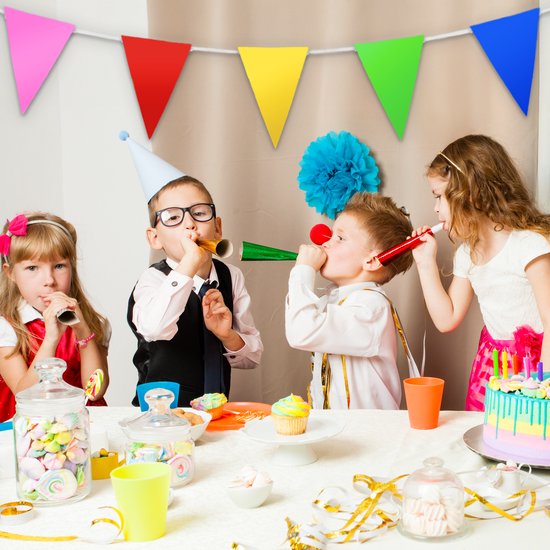 Des enfants soufflent dans des trompettes de fête lors d'un anniversaire avec des fanions colorés et un gâteau.