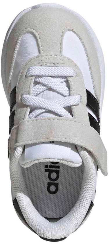 Bovenkant van een witte kindersneaker met grijze suède en zwarte Adidas-strepen, met klittenbandsluiting.