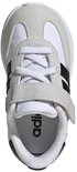 Bovenkant van een witte kindersneaker met grijze suède en zwarte Adidas-strepen, met klittenbandsluiting.