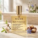 Gouden Huile Prodigieuse multi-purpose dry oil van Nuxe in een glazen fles met gouden dop. Omringd door bloemen en macadamianoten.