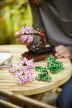Een LEGO Bonsaiboompje met groene bladeren, en roze bloesemtakken ernaast.