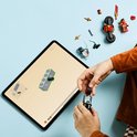 Kind bouwt LEGO speelgoedmotor met tablet, rond ninjafiguren en onderdelen.