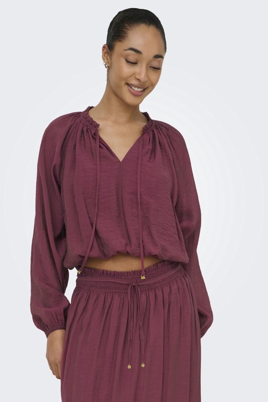 Model draagt een bordeauxrode crop top met pofmouwen en een v-hals met strikdetail.
