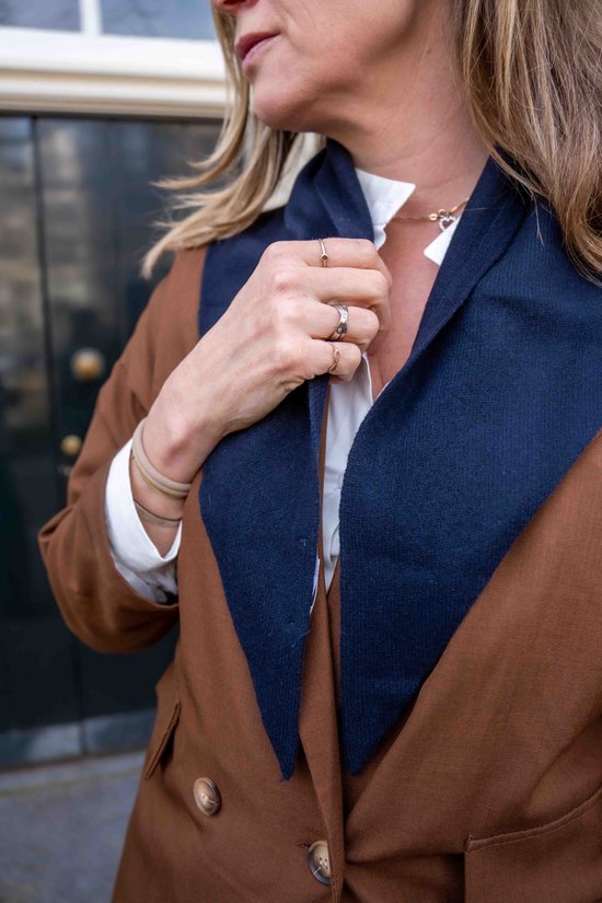 Een vrouw met blond haar draagt een donkerblauwe sjaal over een bruin colbert en wit overhemd.