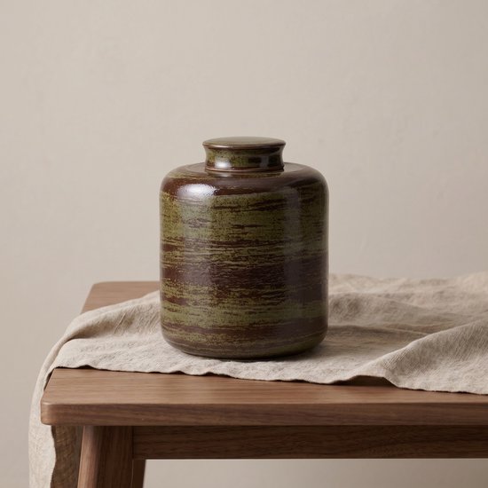 Groene en bruine keramische urn met deksel op tafel.