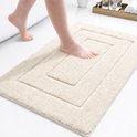 Een beige badmat met een gedempt geometrisch patroon, gezien vanuit een laag perspectief met een voet die erop stapt.