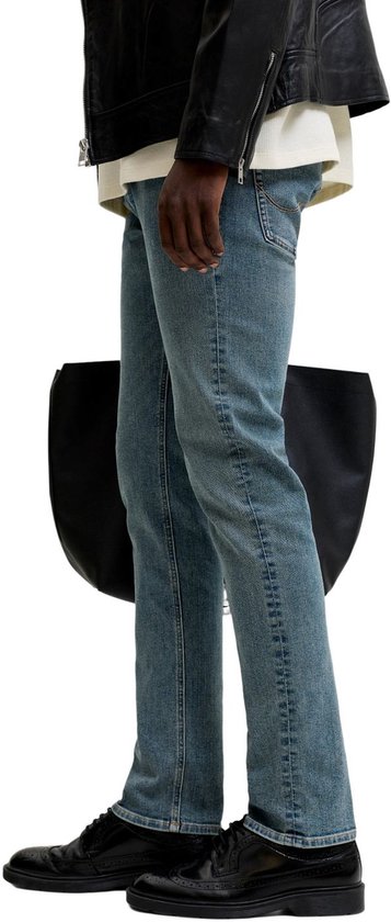 Zijzicht van een man in blauwe slim fit jeans en zwarte schoenen.