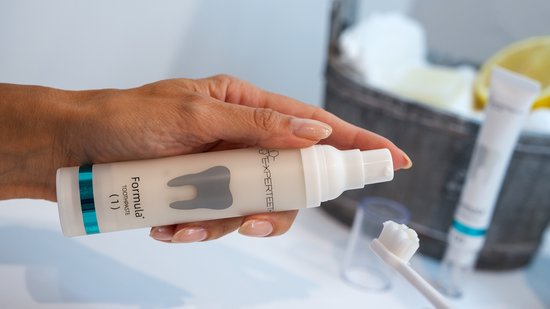 Hand met Experteeth Formula+ tandpastatube, brengt tandpasta aan op borstel.