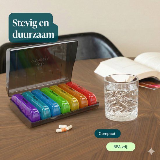 Boîte à pilules arc-en-ciel avec 7 compartiments amovibles, un verre d'eau et des médicaments sur une table.