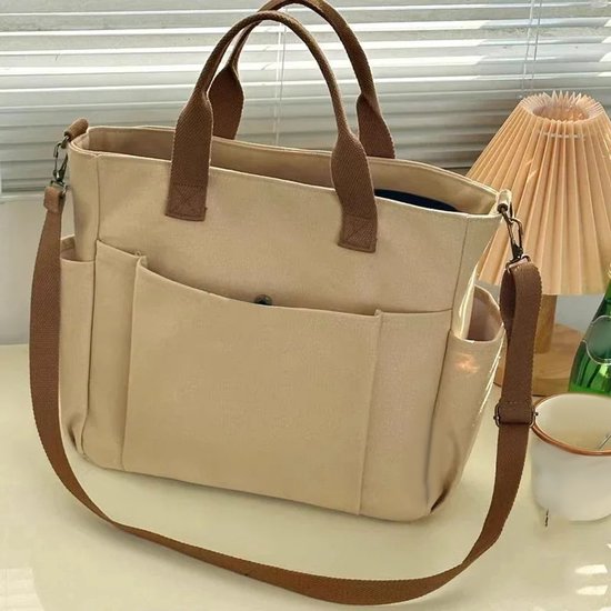 Sac fourre-tout en toile kaki avec des poignées marron, des poches latérales et une longue bandoulière.