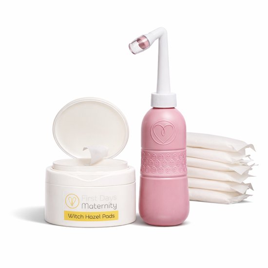 Een roze postpartum spoelfles en een pot witte witch hazel pads, met een stapel extra pads ernaast.