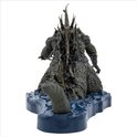 Achterkant van een grijze Godzilla figuur met scherpe rugplaten op een blauwe waterbasis.