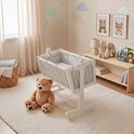 Witte wieg met grijze ruitjes bekleding in een kinderkamer met een teddybeer en een stoffen mand.