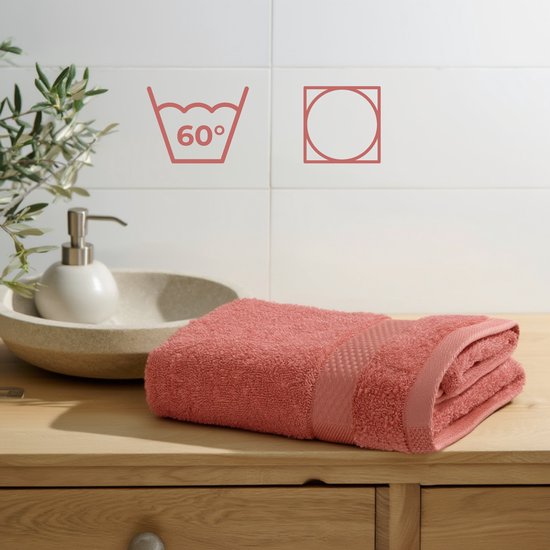 Koraalkleurige handdoek op een houten meubel, met zeepdispenser en plant op de achtergrond.