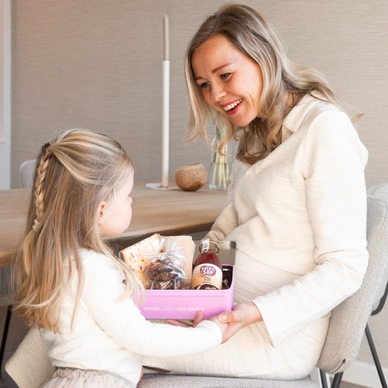 Vrolijke moeder en dochter die samen een roze blik vol lekkers van Zuivelhoeve bekijken.