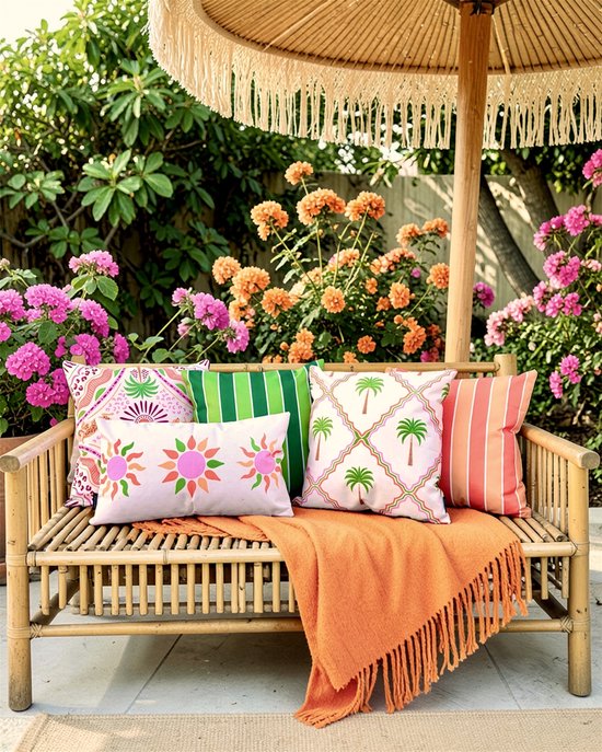 Bamboe bank met veel kleurrijke kussens met palmboom en streepmotieven, met een oranje plaid.