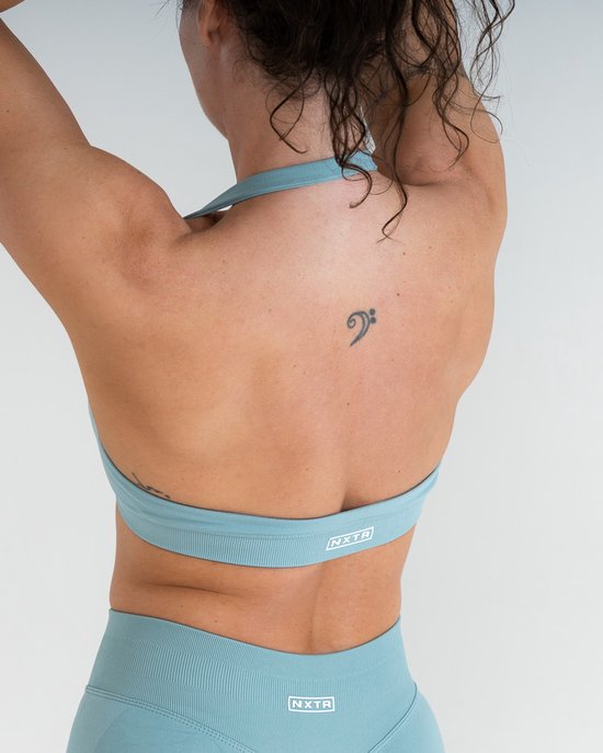 Brassière de sport vert sauge avec le logo NXTR sur la bande.