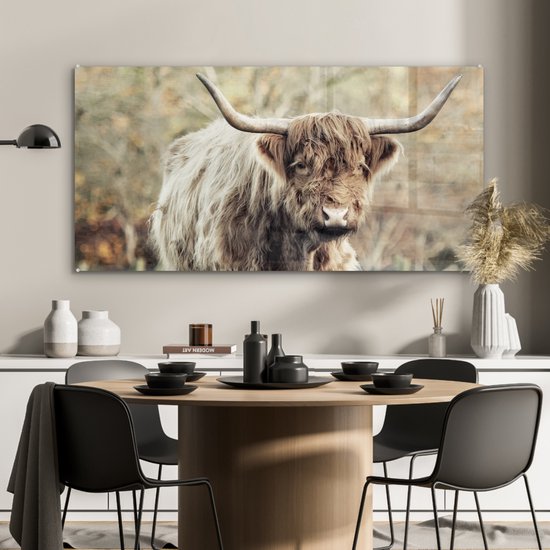 Eetkamer met een glasschilderij van een Schotse Hooglander boven een houten tafel.