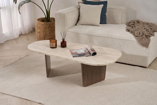 Ovale salontafel met travertin blad en houten poot, met plant en bank op de achtergrond.