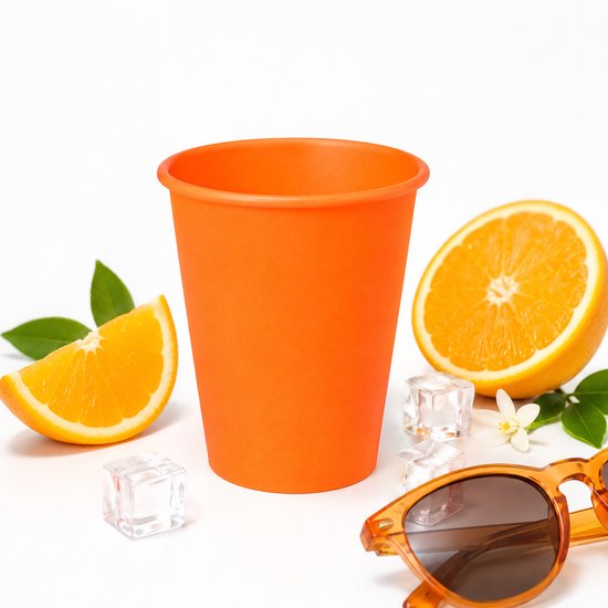 Oranje kartonnen beker met sinaasappelschijfjes, ijsblokjes, een oranje bril en een sinaasappel.