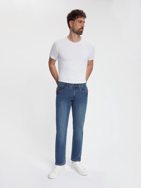 Man in donkerblauwe spijkerbroek, regular fit, met witte sneakers.