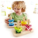 Kind met krullend haar speelt met de Hape vormpuzzel. Stapelt blauwe, groene, roze en gele vormen op houten pegs.