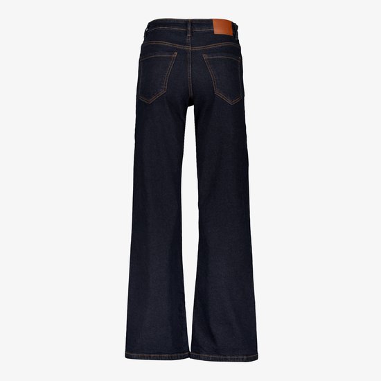 Achterkant van donkerblauwe jeans met wijde pijpen, oranje stiksels en bruin leren label.