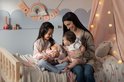 Een vrouw en twee meisjes spelen met een baby-pop in een slaapkamer.
