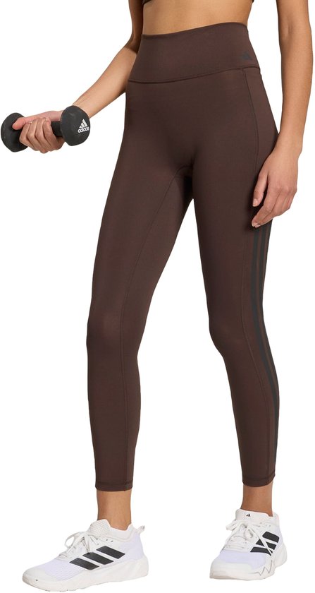Bruine sportlegging met drie zwarte strepen op het linkerbeen. Gedragen door een vrouw met een halter.