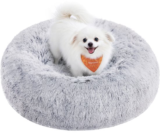 Kleine witte hond met oranje bandje staat in een ronde, grijze, pluizige hondenmand.