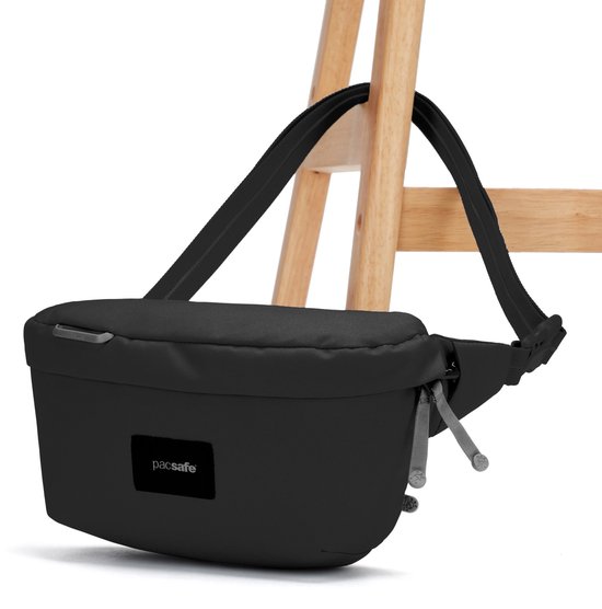 Zwarte Pacsafe sling tas met verstelbare band, hangend aan een houten stoel.