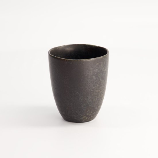 Tasse noire avec une surface rugueuse et tachetée et un léger éclat, vue de trois quarts avant.