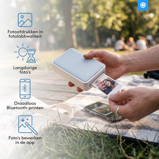 Een persoon print een foto van een ouder echtpaar met een Silvergear printer, zittend in het gras met een telefoon ernaast.