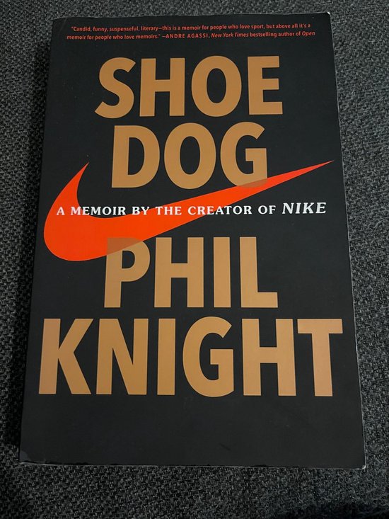 Livre "Shoe Dog" avec le logo swoosh Nike en orange et rouge. Le texte est beige et blanc.